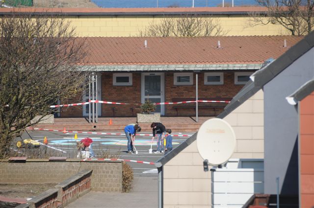 Aus der Entfernung: Schüler stehen gebückt und streichen den Boden des Schulhofs an.