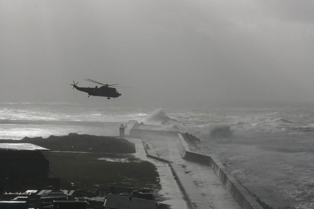Ein großer Hubschrauber der Bundeswehr schwebt bei Sturm über dem Wellensturzbecken Helgolands.