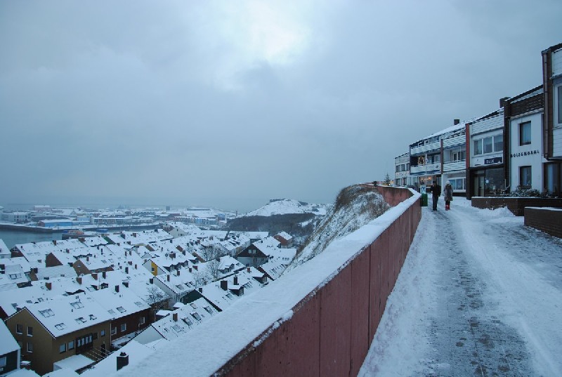 Blick über den und am Falm entlang, der das mit Schnee bedeckte Helgoland zeigt.