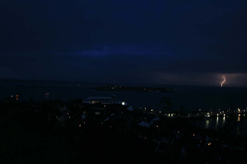 Nachtaufnahme von Helgoland aus mit einem Blitz über dem Festland.