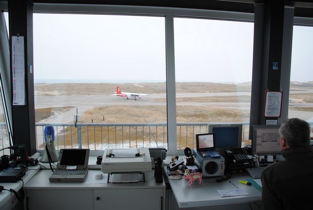 Blick aus den schräg gestellten Fensterscheiben des Towers auf der Helgoländer Düne während ein Flugzeug auf der Rollbahn fährt.