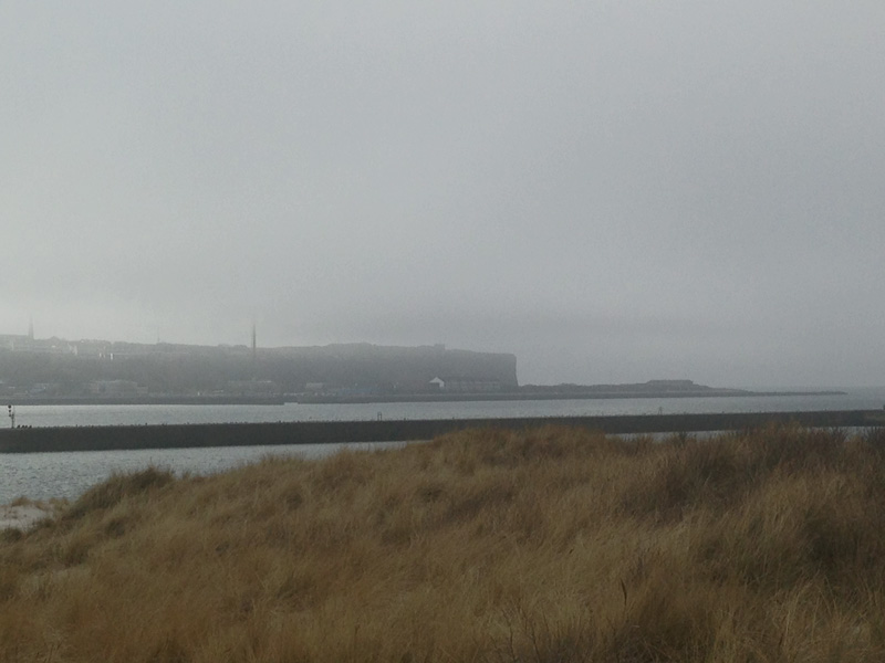 von der Düne aus gesehen ist Helgoland im Hintergrund und von Norden schiebt sich Seenebel zwischen Helgoland und Düne.