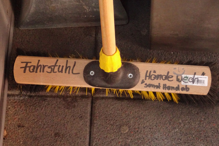 Ein Besen lehnt an der Wand im Einstiegsbereich des Fahrstuhls im Oberland mit der handschriftlichen Aufschrift Hände wech, sonst Hand ab.