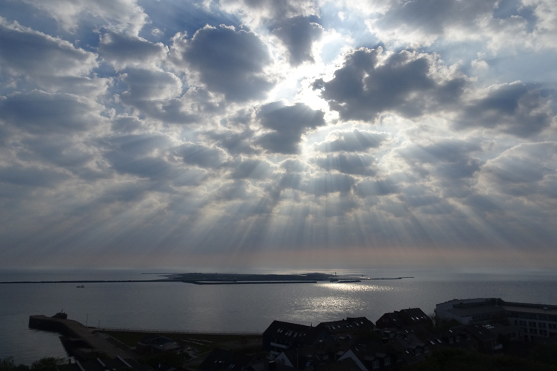 Wolkenspiel über der Düne morgens um acht mit vielen Wolkenstrahlen die sich fast wie ein Schirm über die Düne spannen.