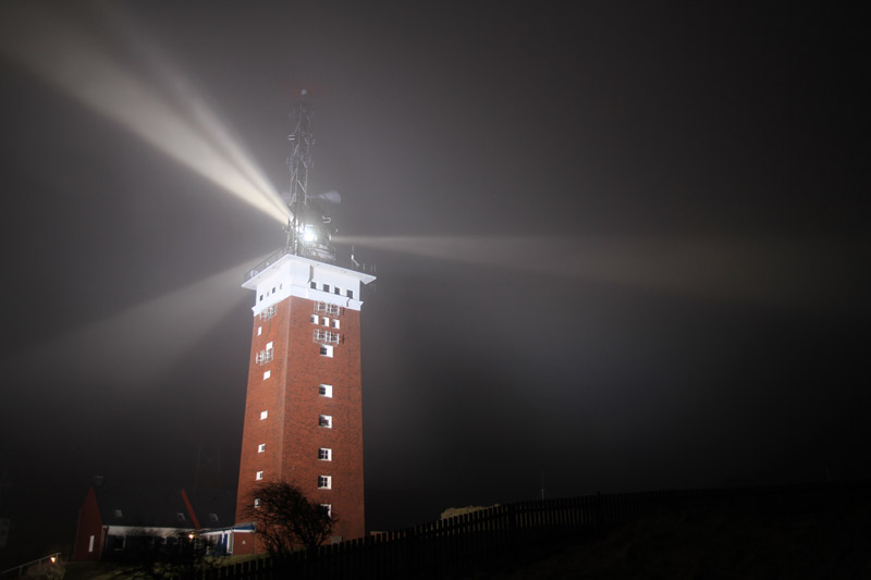 Helgolands Leuchtturm nachts in grellem Scheinwerferlicht.