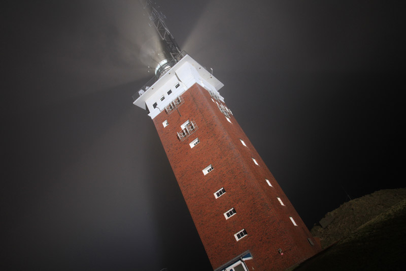 Helgolands Leuchtturm nachts in grellem Scheinwerferlicht.