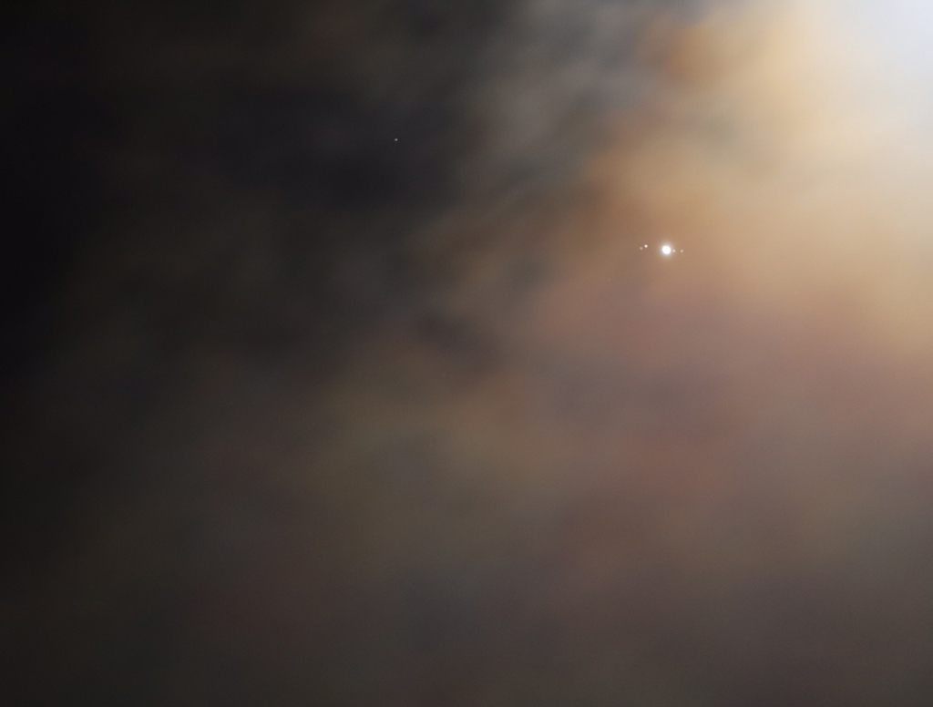Jupiter und seine vier größten Monde durch irisierende Wolken von Helgoland aus gesehen.