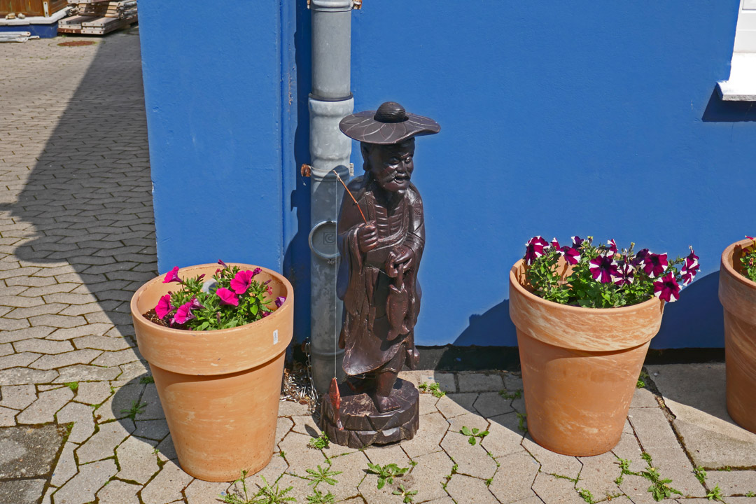Bepflanzte Blumentöpfe und eine Skulptur in einer Gasse vor einem Helgoländer Haus.