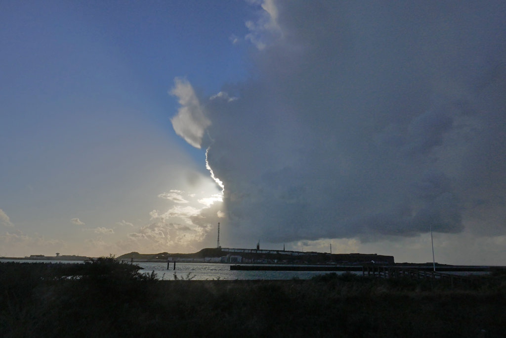 Ein hochaufragende Wolke mit scharfer, senkrechter Kante schwebt mittig über Helgoland und teilt den Himmel in wolkenverhangenen und blauen Himmel.