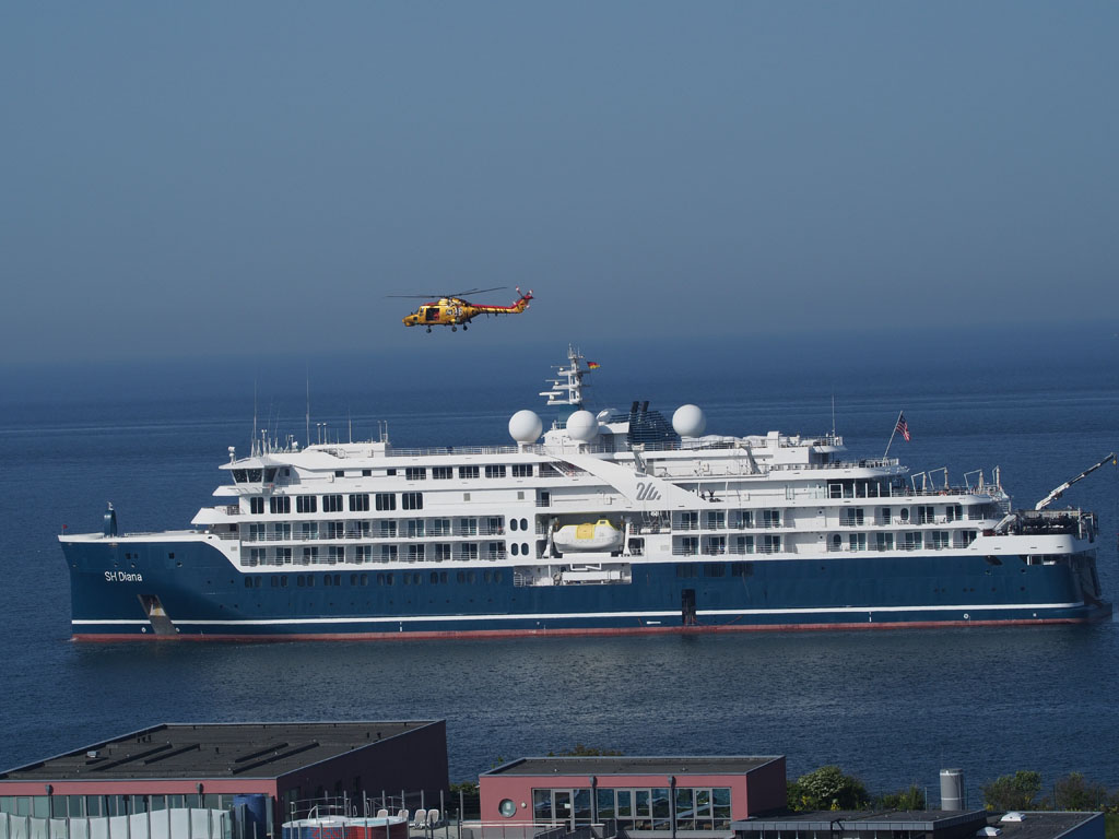 Kreuzfahrtschiff SH Diana ankert auf dem Fahrwasser vorm Schwimmbad auf Helgoland und ein MK88a Sea Lynx Hubschrauber &uuml;berfliegt sie.