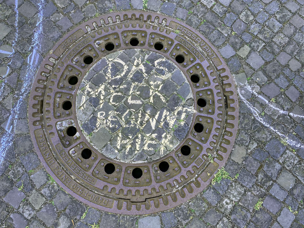 Auf Helgoland ist mit gelber Kreide auf einem Kanaldeckel geschrieben: DAS MEER BEGINNT HIER.