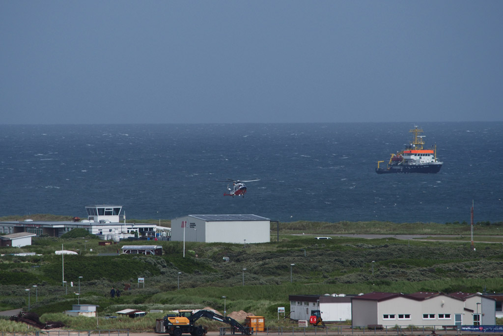 Ein Hubschrauber landet auf dem Flugplatz auf der D&uuml;ne vom Falm aus gesehen.