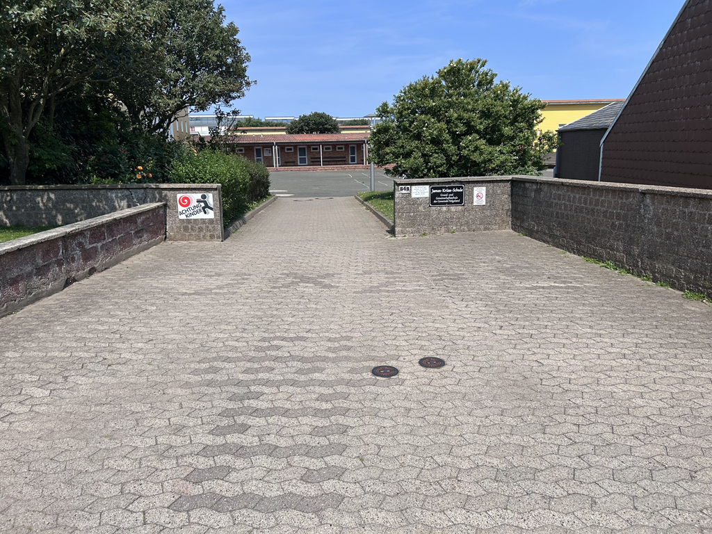 Durch dunkleres Pflaster gelegter Schriftzug 2+2= vor der Schule auf Helgoland.