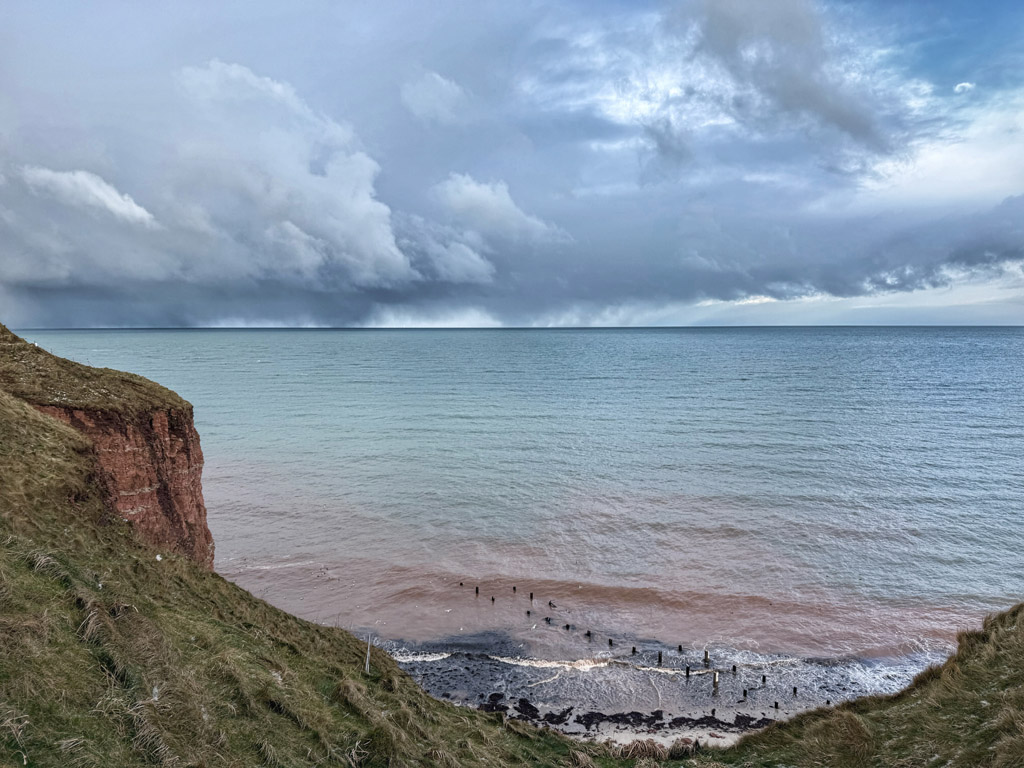 Blick &uuml;ber Helgolands Klippenrand und &uuml;bers Meer bis zum Horizont bei wolkenreichem Himmel.
