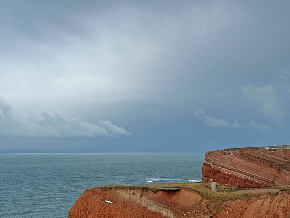 Die Westseite Helgolands entlang gesehen mit der Nebelkuh auf der Nordmole im Hintergrund.