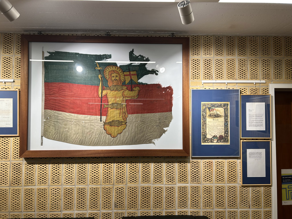 Die in einem verglasten Rahmen ausgestellte Helgolandflagge mit Nikolaus, dem Schutzpatron Helgolands.