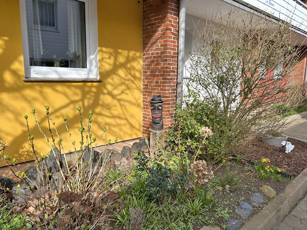 Eine Blumenbeet mit einer Holzskulptur-B&uuml;ste vor einem Haus im Unterland auf Helgoland.